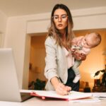 मातृत्व के बाद करियर में वापसी करती हुई एक भारतीय महिला, लैपटॉप पर काम करती हुई और बच्चे की देखभाल के बीच संतुलन बनाते हुए।