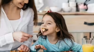 “माता-पिता अपने बच्चे को सब्ज़ियाँ और फल खिलाते हुए, हेल्दी और मजेदार तरीके से।