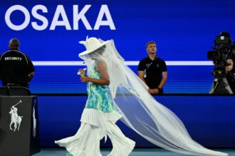 ऑस्ट्रेलियन ओपन के कोर्ट पर टेनिस खेलती नाओमी ओसाका, सफ़ेद “जेलीफ़िश ड्रेस” में, जो मातृत्व और भावनात्मक अभिव्यक्ति से प्रेरित एक अनोखा स्पोर्ट्स फैशन लुक दर्शाती है।
