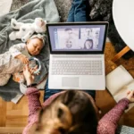 वर्क-फ्रॉम-होम करती एक कामकाजी माँ, जो लैपटॉप पर काम करते हुए बच्चे की देखभाल कर रही है, करियर और परिवार के बीच संतुलन दर्शाती हुई।