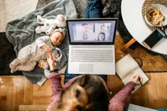 वर्क-फ्रॉम-होम करती एक कामकाजी माँ, जो लैपटॉप पर काम करते हुए बच्चे की देखभाल कर रही है, करियर और परिवार के बीच संतुलन दर्शाती हुई।