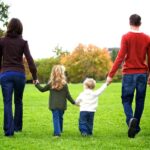 हरे-भरे पार्क में माता-पिता अपने दो बच्चों का हाथ थामे साथ चलते हुए, खुशहाल परिवार की झलक