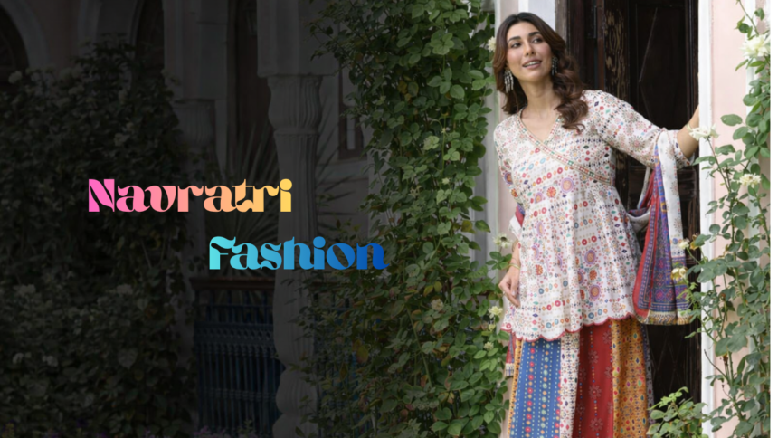 एक खूबसूरत साउथ एशियन महिला पारंपरिक घर के दरवाजे पर खड़ी है, चारों तरफ हरियाली और फूल हैं। उसने मल्टीकलर प्रिंटेड कुर्ता, स्कर्ट और दुपट्टा पहना हुआ है। बाईं ओर “Navratri Fashion” लिखा हुआ है।