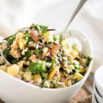 Fresh mango-cucumber rice salad served in a white bowl, mixed with herbs, nuts, and colorful vegetables for a healthy summer meal.
