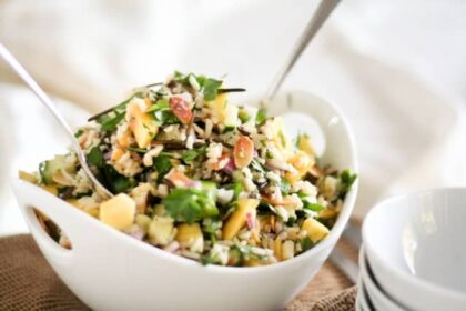 Fresh mango-cucumber rice salad served in a white bowl, mixed with herbs, nuts, and colorful vegetables for a healthy summer meal.