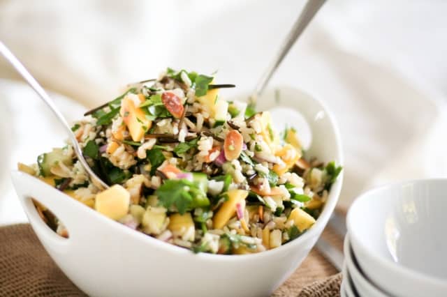 Fresh mango-cucumber rice salad served in a white bowl, mixed with herbs, nuts, and colorful vegetables for a healthy summer meal.