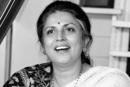 काले-सफेद (Black & White) पोर्ट्रेट में एक महिला मुस्कुराते हुए दिखाई दे रही हैं। उन्होंने साड़ी पहन रखी है, माथे पर बिंदी है और बाल पीछे की ओर बंधे हुए हैं। तस्वीर में उनका चेहरा आत्मविश्वास, सादगी और सौम्यता को दर्शाता है। बैकग्राउंड में घर का इंटीरियर दिखाई दे रहा है, जिससे यह एक अनौपचारिक और स्वाभाविक क्षण की तस्वीर लगती है।