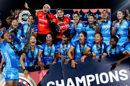 भारतीय महिला हॉकी टीम FIH Women’s Nations Cup जीतने के बाद ट्रॉफी और पदकों के साथ मंच पर जश्न मनाती हुई दिखाई दे रही है। खिलाड़ी खुशी से उत्साहित होकर "Champions" बोर्ड के सामने जीत का उत्सव मना रही हैं।