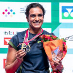 PV Sindhu smiles while holding her gold medal and winner's trophy after winning the Japan Open 2026 badminton championship.