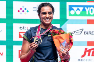 PV Sindhu smiles while holding her gold medal and winner's trophy after winning the Japan Open 2026 badminton championship.