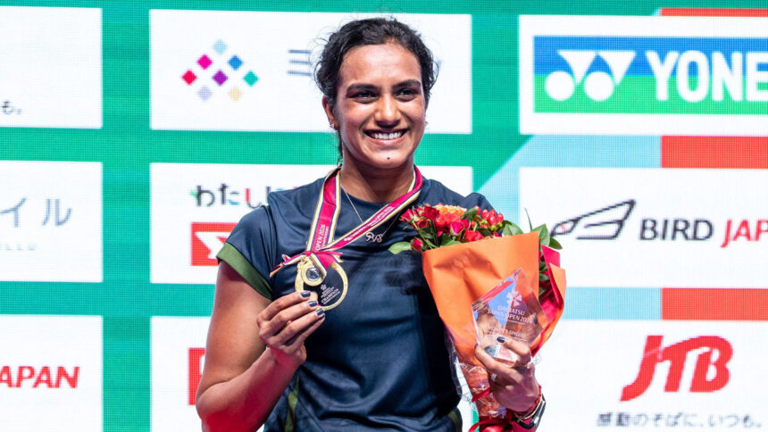 PV Sindhu smiles while holding her gold medal and winner's trophy after winning the Japan Open 2026 badminton championship.