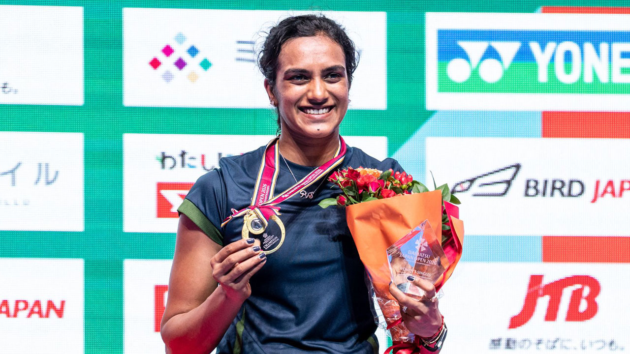 PV Sindhu smiles while holding her gold medal and winner's trophy after winning the Japan Open 2026 badminton championship.