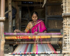 An Indian woman weaving a colorful silk fabric on a traditional handloom inside a rural weaving workshop.