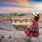 Woman in colorful dress standing at an ancient amphitheater during sunset