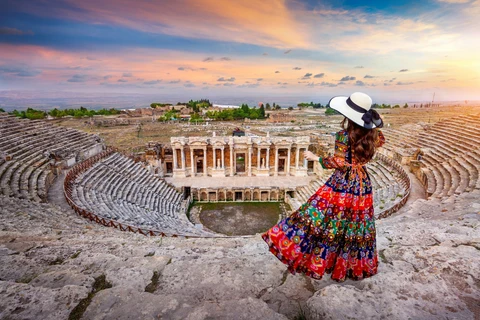Woman in colorful dress standing at an ancient amphitheater during sunset
