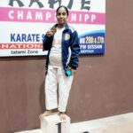V. Anita standing on the first-place podium holding her gold medal at a karate championship.
