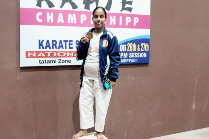 V. Anita standing on the first-place podium holding her gold medal at a karate championship.