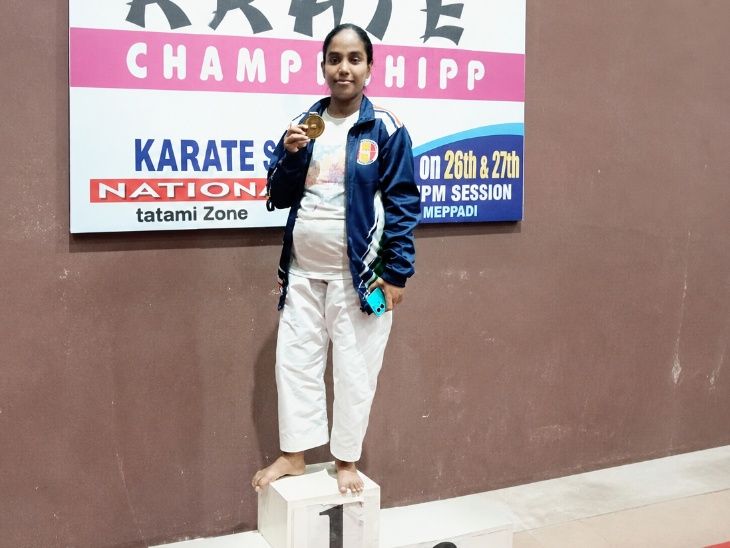 V. Anita standing on the first-place podium holding her gold medal at a karate championship.