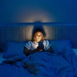 Woman using a smartphone in bed at night, highlighting the impact of screen light on sleep