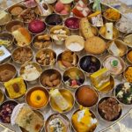 A beautifully arranged traditional Indian sweet platter featuring assorted mithai, dry fruits, and festive delicacies in small golden bowls.