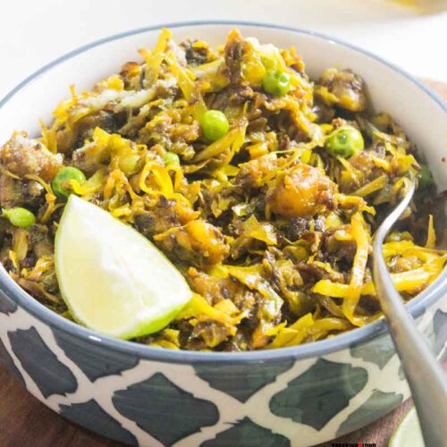 Traditional Bengali cabbage and green peas curry served in a bowl with lemon wedge.